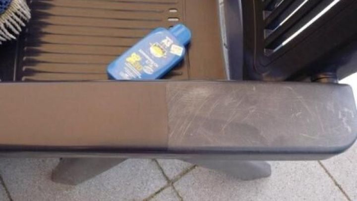 Ein dunkler Kunststoffgartenstuhl mit ausgeblichenem und renoviertem Bereich; daneben liegt eine blaue Flasche mit Sonnensymbol.