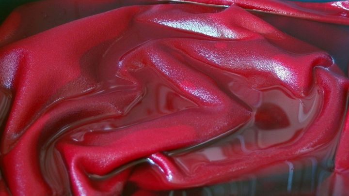 Ein rotes T-Shirt liegt zerknittert in einer transparenten Umgebung, wahrscheinlich in einer Waschmaschine oder auf einer Abstellfl&auml;che.