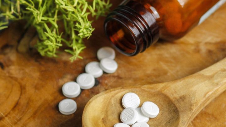 Wei&szlig;e Sch&uuml;sslersalze liegen auf einem Holzl&ouml;ffel, w&auml;hrend die Flasche und frische Kr&auml;uter im Hintergrund sichtbar sind.