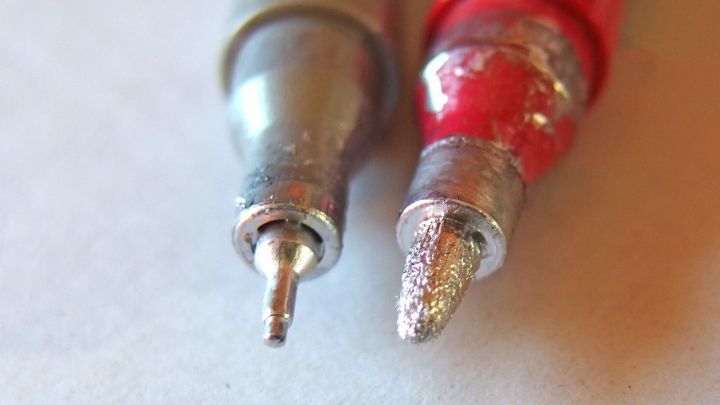 Ein Lackmalstift liegt nebeneinander mit einem eingetrockneten Ende, w&auml;hrend das andere eine besch&auml;digte Spitze zeigt.