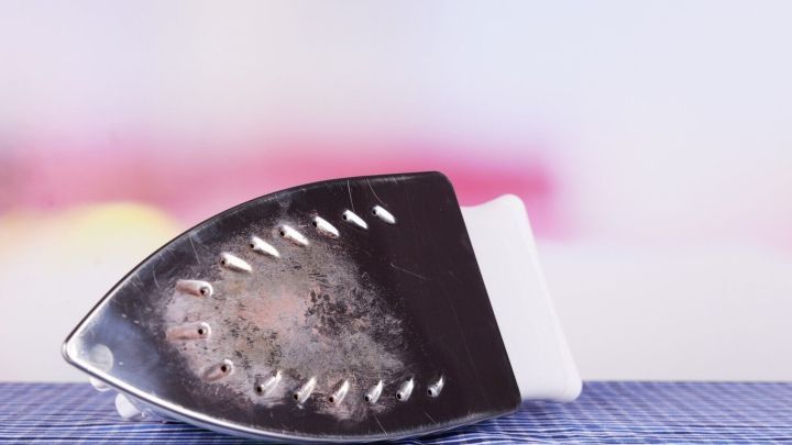 Ein stark verschmutztes B&uuml;geleisen liegt auf einem blauen Tuch, bereit zur Reinigung in einem hellen, unscharfen Raum.