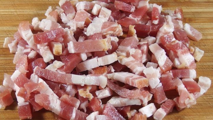 St&uuml;ckchen frischen Specks liegen auf einem Holzbrett, vorbereitet zum Schneiden f&uuml;r die Zubereitung von Gerichten.