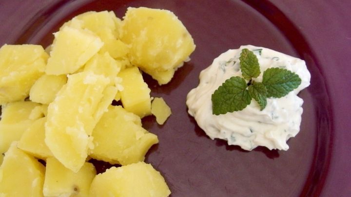 Gekochte Pellkartoffeln neben einem Kr&auml;uterquark, garniert mit Minze, auf einem dunklen Teller angerichtet.