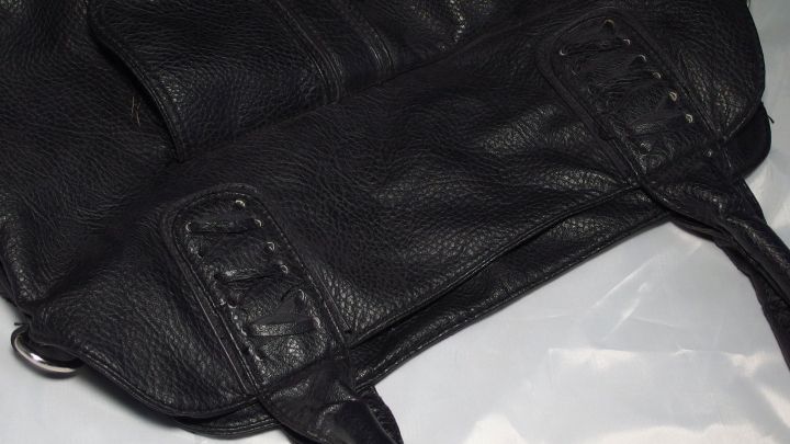 Eine schwarze Ledertasche liegt auf einer hellen Oberfl&auml;che, w&auml;hrend sie mit Melkfett gepflegt wird, um die Haut zu sch&uuml;tzen.