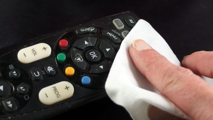 Eine Hand reinigt mit einem Tuch eine schmutzige Fernbedienung, um sie wieder sauber zu machen.