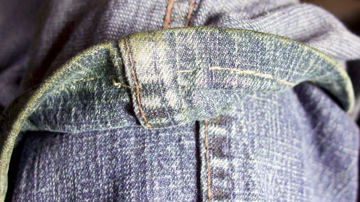 Ein Jeanskragen mit Grasflecken wird in einer Nahaufnahme gezeigt. Im Hintergrund ist eine weitere Jeans sichtbar.