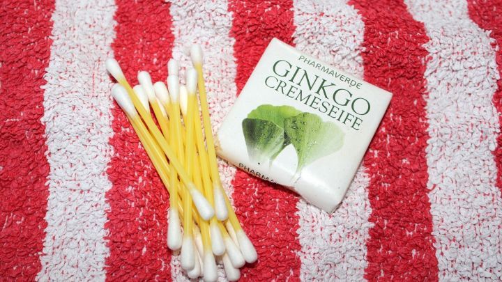 Eine Ginkgo-Cremeseife liegt neben Baumwattest&auml;bchen auf einem gestreiften Handtuch. Juckreiz bei Insektenstichen wird behandelt.