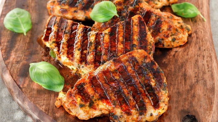 Gegrillte Pute liegt auf einem rustikalen Holzbrett, umgeben von frischem Basilikum, appetitlich und hochwertig angerichtet.