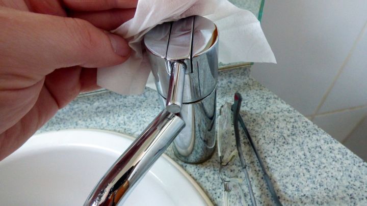 Ein Brillenputztuch wird benutzt, um die gl&auml;nzende Oberfl&auml;che einer Badarmatur zu reinigen, w&auml;hrend es in einem Badezimmer ist.