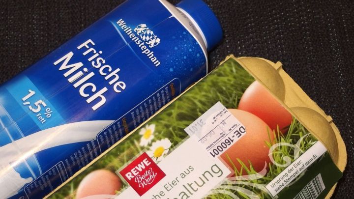 Eine Packung frischer Milch steht neben einem Karton mit Eiern auf einem dunklen Hintergrund, bereit zum Einkauf im Supermarkt.