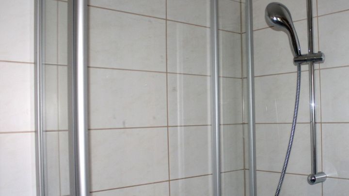Eine Duschkabine mit glatten W&auml;nden und einem Duschkopf, die bereit ist, um Kalkablagerungen zu reduzieren, steht im Badezimmer.