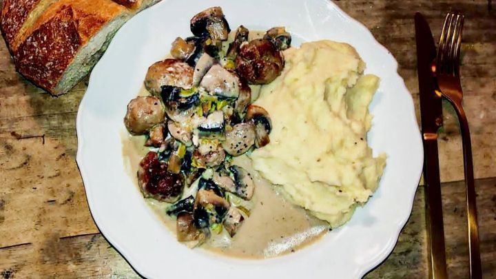 Kartoffelbrei mit Wasabi liegt auf einem wei&szlig;en Teller, daneben sind Fleischb&auml;llchen und frisches Brot auf einem Holztisch.