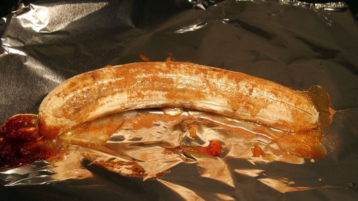 Eine gegrillte Banane liegt auf Aluminiumfolie, &uuml;berzogen mit Honig und Schokolade, bereit f&uuml;r den Genuss im Freien.