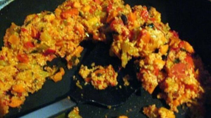 In einer Pfanne liegt bunter Paprika-Mango-Couscous, leicht angebraten und vermischt, umgeben von einer dunklen K&uuml;chenumgebung.