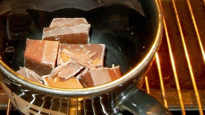 Im schwarzen Becher schmelzen St&uuml;cke von Blockschokolade auf einem Gitterrost, um leckere Kuvert&uuml;re zuzubereiten.