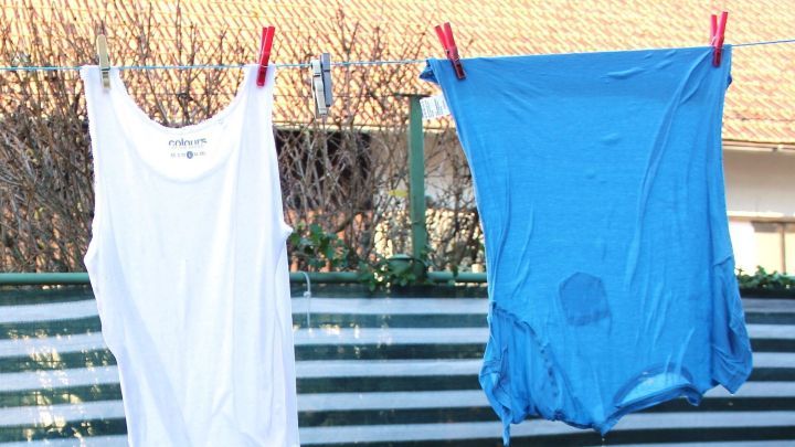 Ein wei&szlig;es und ein blaues Kleidungsst&uuml;ck h&auml;ngen an einer W&auml;scheleine, leicht feucht und umgeben von einem klaren Himmel.