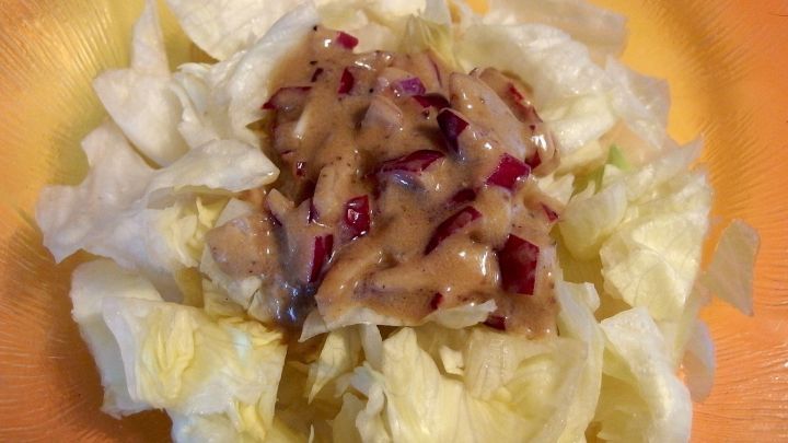 Eisbergsalat ist in verschiedenen Varianten angerichtet und mit einer cremigen Salatsauce &uuml;berzogen, auf einem orangefarbenen Teller.