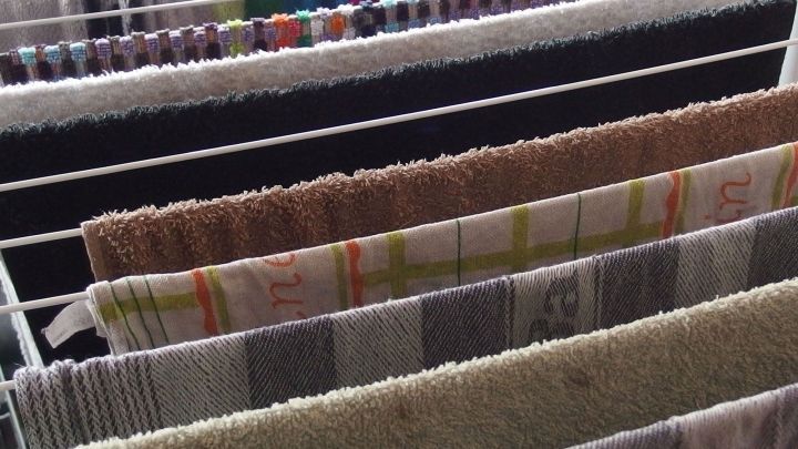 Handt&uuml;cher h&auml;ngen zum Trocknen auf einem W&auml;schest&auml;nder, umgeben von weiteren bunten Textilien in einem Innenraum.