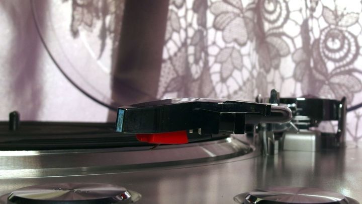 Ein Plattenspieler steht auf einem Tisch und wird mit einer sanften Bewegung bedient, w&auml;hrend ein Vorhang im Hintergrund h&auml;ngt.