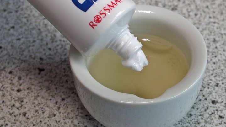 Eine Tube Zahnpasta wird &uuml;ber eine kleine Sch&uuml;ssel mit einer gelben Fl&uuml;ssigkeit ausgegossen, um eine Anti-Pickel-Creme herzustellen.