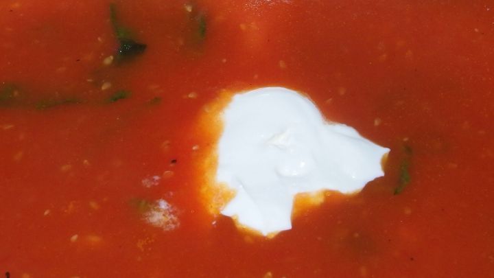 Eine leuchtend rote Tomatenso&szlig;e mit einem Klecks Sahne in der Mitte, serviert in einer Sch&uuml;ssel auf einem Tisch.