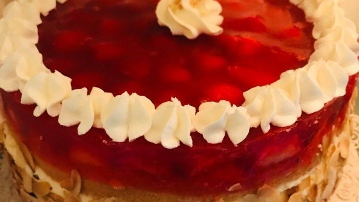 Ein runder, saftiger Tortenboden wird von einer gl&auml;nzenden Fruchtglasur und Sahne verziert, in einer hellen K&uuml;che.