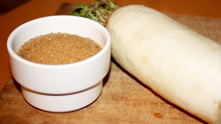 Ein Rettich liegt neben einer wei&szlig;en Sch&uuml;ssel mit Zucker auf einem Holzbrett, bereit zur Zubereitung eines Hustenl&ouml;ser.