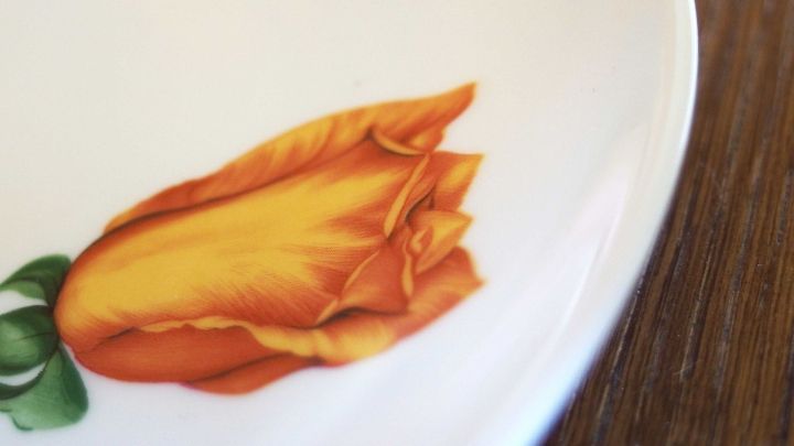 Ein Geschirrst&uuml;ck mit einer orangefarbenen Bl&uuml;tenmalerei liegt auf einem Holzuntergrund. Es zeigt keine grauen Streifen.