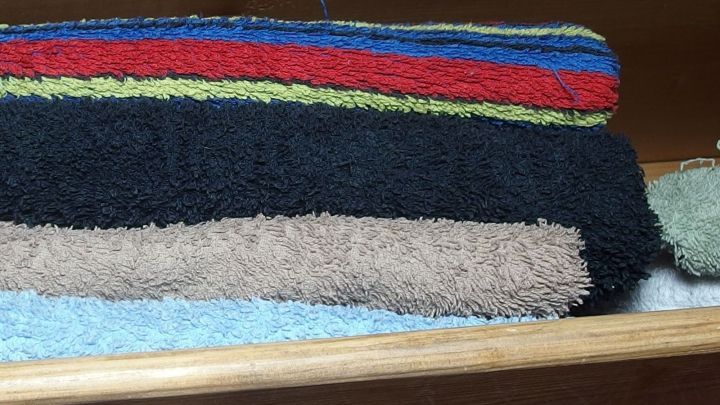 Hochgestapelte Handt&uuml;cher werden ordentlich im oberen Schrank verstaut, um Platz f&uuml;r kleinere Personen zu schaffen.