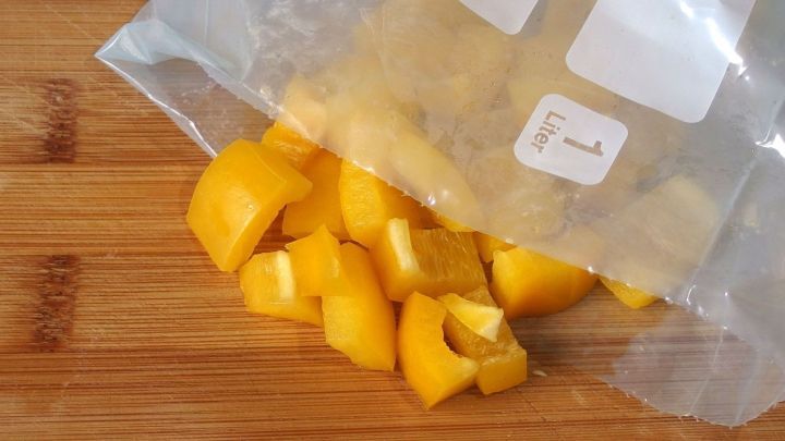 In einer durchsichtigen Plastikt&uuml;te liegen frische, gew&uuml;rfelte Paprikaschoten auf einem Holzbrett, bereit zum Einfrieren.