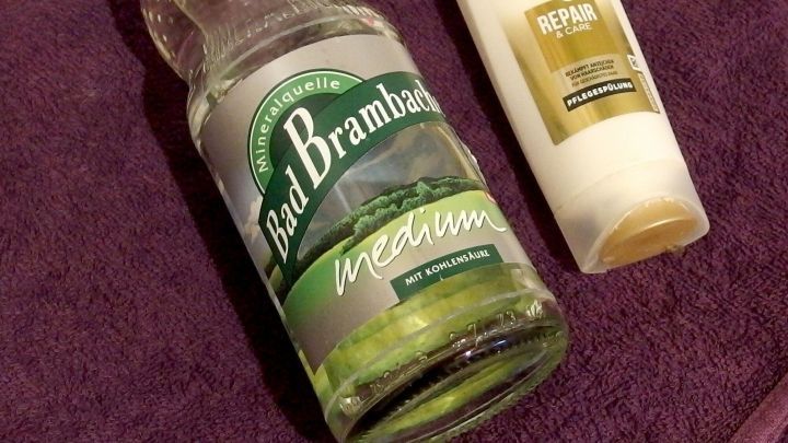 Eine Flasche Mineralwasser liegt neben einer Haarsp&uuml;lung auf einem lila Handtuch, bereit zur Anwendung f&uuml;r verbesserte Haarpflege.