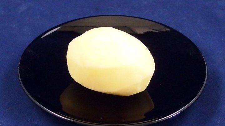 Eine rohe Kartoffel liegt auf einem schwarzen Teller auf einem blauen Tisch, die zur Linderung von Sodbrennen empfohlen wird.