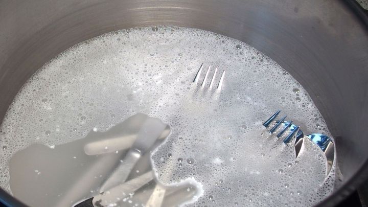 Gl&auml;nzendes Besteck liegt in einem Topf mit sch&auml;umendem Wasser und Waschpulver, das zum Reinigen vorbereitet ist.