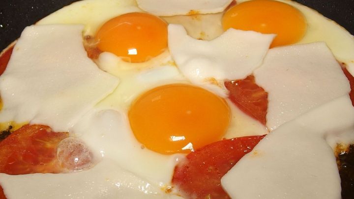 Spiegeleier werden in einer Pfanne mit Schinken und K&auml;se zubereitet, um ein herzhaftes italienisches Fr&uuml;hst&uuml;ck zu kreieren.