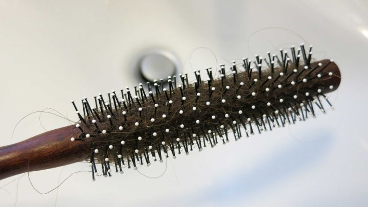 Eine Rundb&uuml;rste mit Haaren h&auml;ngt &uuml;ber einem Waschbecken, wo sich ein Abfluss befindet. Haare in Abfluss entfernen.