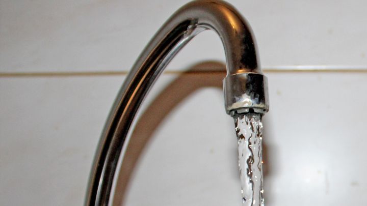 Ein Wasserhahn sprudelt frisches Leitungswasser, das in einem modernen Badezimmer aus gl&auml;nzenden Fliesen flie&szlig;t.