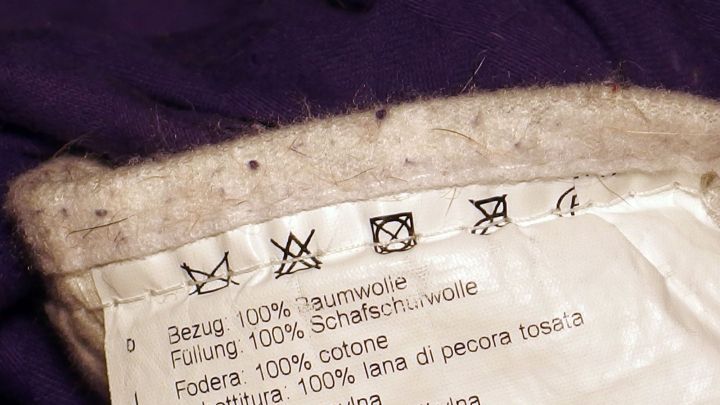 Pflegehinweise auf einem Textiletikett zeigen Waschsymbole und Materialzusammensetzung f&uuml;r die Reinigung von Kleidung.
