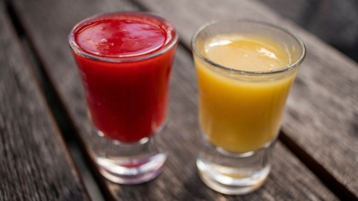 Zwei Gl&auml;ser mit rotem und gelbem Getr&auml;nk stehen auf einem Holztisch, ideal f&uuml;r hei&szlig;e Tage oder gesellige Abende.