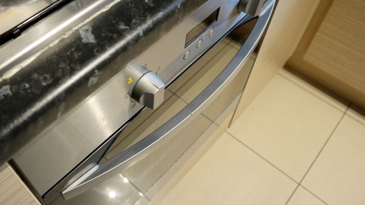 Ein gl&auml;nzender Edelstahlofen mit einer modernen Griffleiste steht in einer modernen, hellen K&uuml;che auf Fliesen.