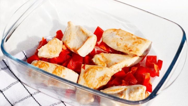 H&uuml;hnchenst&uuml;cke liegen in einer Glasform auf gew&uuml;rfelten Paprika, bereit zum Garen in einer w&uuml;rzigen Rahmsauce.