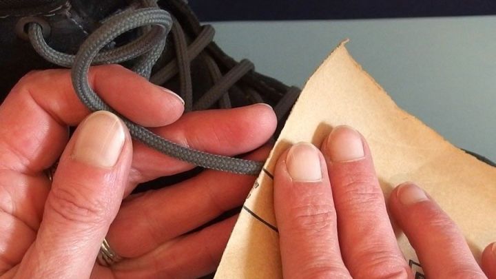 Ein Paar H&auml;nde f&auml;deln einen Schuhband durch ein Loch in einem St&uuml;ck Papier, um die Schn&uuml;rsenkel zu verbessern.