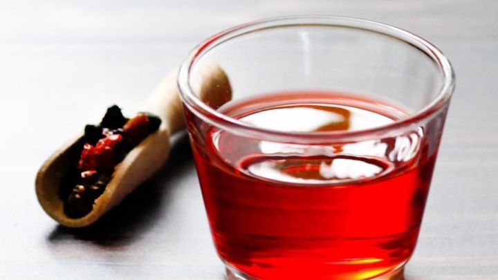 Ein Glas roter Preiselbeersaft steht auf einem Holzuntergrund, neben einer kleinen Rolle mit Preiselbeeren.