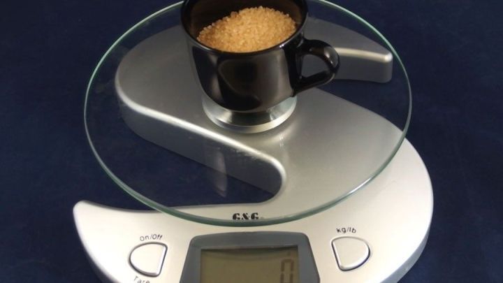 Ein schwarzer Becher mit braunem Zucker wird auf einer digitalen Waage gewogen, um genaue Ma&szlig;e zu erhalten.