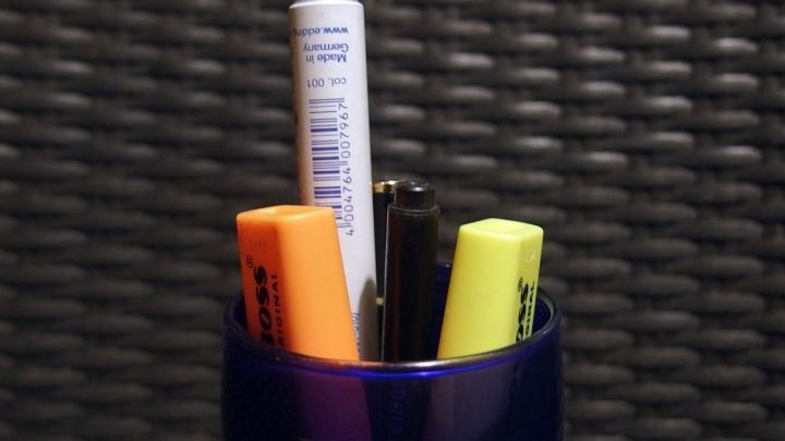 Ein Stiftbeh&auml;lter mit Textmarkern und Kugelschreibern steht auf einem dunklen, strukturierten Tisch.