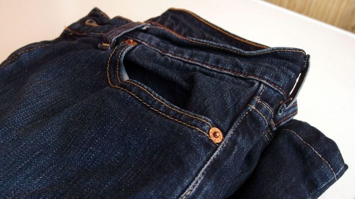 Eine gefaltete, dunkle Jeans liegt ordentlich auf einem Tisch, um den Klebstoff von der Kleidung zu entfernen.