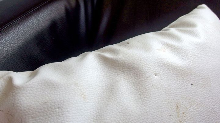 Ein Kissen liegt auf einem dunklen Sofa, die Oberfl&auml;che ist zerknittert und hat kleine Flecken, was seine Praktikabilit&auml;t beeintr&auml;chtigt.