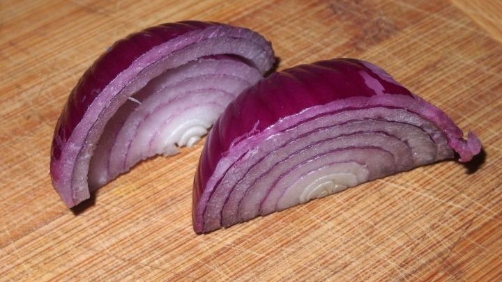 Rotzwiebeln sind in zwei gleichm&auml;&szlig;ige H&auml;lften geschnitten und liegen auf einem Holzbrett. Der geschnittene Teil zeigt die schichtenartige Struktur.