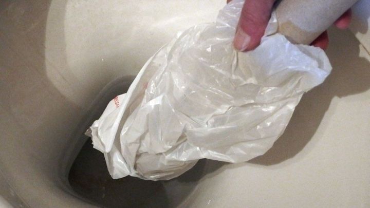 Eine Hand h&auml;lt eine gefaltete Plastik-T&uuml;te &uuml;ber die Toilette, w&auml;hrend die Toilette verstopft ist, ohne Saugglocke zur Hand.