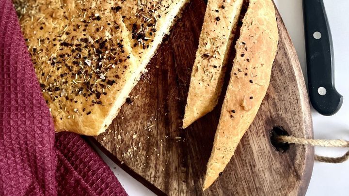 D&uuml;nnes Fladenbrot liegt auf einem Holzbrett, frisch geschnitten, umgeben von einem roten Tuch und einem K&uuml;chenmesser.