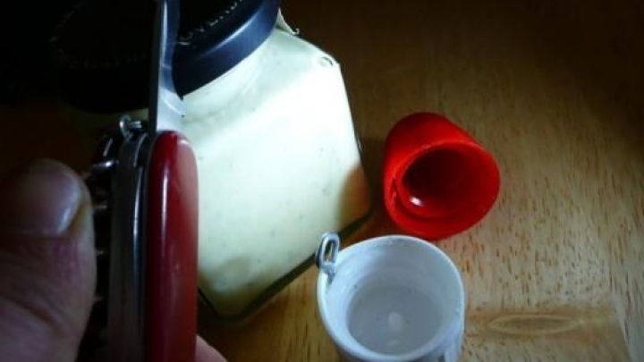 Ein Schraubglas wird mit einem Taschenmesser ge&ouml;ffnet. Daneben liegt ein roter, kindersicherer Deckel auf einem Holztisch.